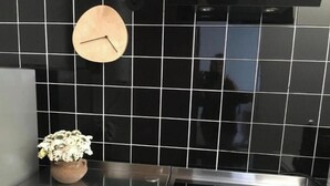 Eine Küche mit schwarzem Fliesenrückwand, einer Holzuhren und einem Blumentopf auf der Arbeitsplatte.