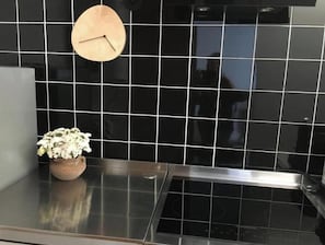 A kitchen with black tiled backsplash, a wooden clock, and a potted plant on the counter. - Pedra do Sal House (Estoril)