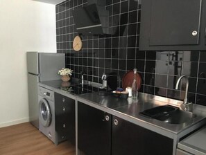 Eine kleine Küche mit Waschmaschine, Spüle und einer Uhr an der Wand.