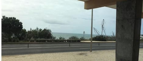 Un espacio al aire libre techado con un sendero pavimentado, vista al mar y una carretera al fondo.