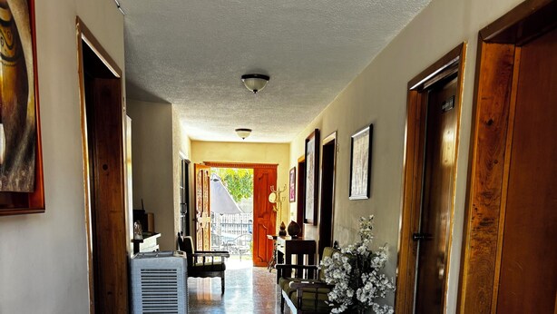 A hallway with a polished stone floor, wooden furniture, and a door leading to an outdoor area. - HOTEL FRANCO (El Fuerte)
