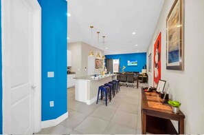 Eine moderne Küche mit blauer Akzentwand, einer zentralen Kochinsel mit Sitzgelegenheiten, Pendelleuchten und einem Essbereich mit Bar.