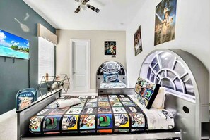 Ein Schlafzimmer mit Bettdecke im Star-Wars-Design, einem Fenster mit Aussicht und einem Deckenventilator.