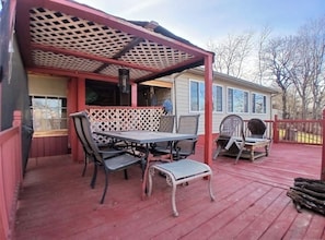 A covered outdoor patio with a table and chairs, a covered seating area, and a house in the background.