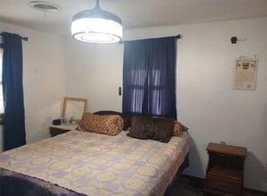 A bedroom with a bed, a nightstand, a dresser, a ceiling light, and a window with curtains.