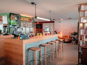 A bar area with stools, a coffee machine, and shelves with bottles. - Premiere Classe Montpellier EST Parc Expo Aeroport (Mauguio)