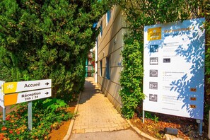 A pathway leading to a hotel entrance with a reception sign indicating 24-hour reception. - Premiere Classe Montpellier EST Parc Expo Aeroport (Mauguio)