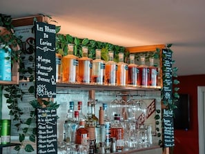 Et barområde med hylder fyldt med spiritusflasker og en tavlemenu med drikkevarer.