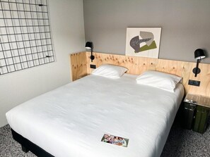 A hotel room with a wooden headboard, two bedside tables, a bed with white linens, a wall-mounted artwork, and a window with a grid pattern. - Greet Hotel Montpellier Aéroport Parc des Expos (Mauguio)
