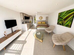 Ein modernes Wohnzimmer mit Fernseher, Glastisch und zwei Sesseln.