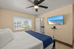 A bedroom with a bed, a ceiling fan, a TV on the wall, and a window with blinds.