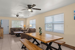 A dining area with a wooden table, benches, a ceiling fan, and a couch.