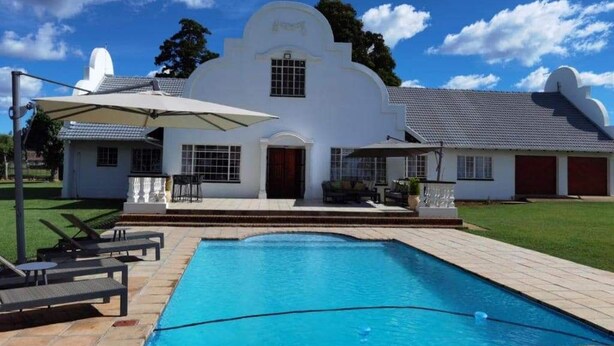 A white building with a pool, outdoor furniture, and a clear sky.