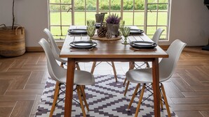 A dining area with a wooden table, white chairs, and a patterned rug.