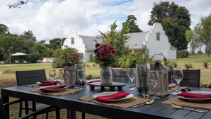 An outdoor dining table set with red napkins, clear glasses, and a vase with flowers.