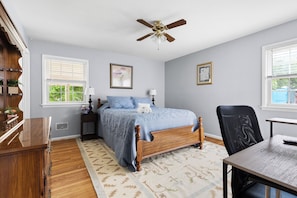 A bedroom with a bed, a desk, a chair, a ceiling fan, and two windows. - Charming 3-bedroom house with AC in Raleigh for your stay (Raleigh)