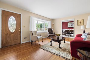 A living room with a wooden door, a dining area with a table and chairs, and a red sofa.