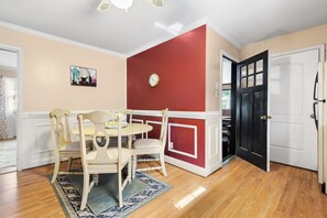 A dining area with a round table, four chairs, a clock, and a door.