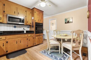 A kitchen with wooden cabinets, a microwave, an oven, and a dining area with a table and chairs. - Charming 3-bedroom house with AC in Raleigh for your stay (Raleigh)