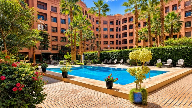 Ein Hotelinnenhof mit Swimmingpool, Palmen und Liegestühlen.