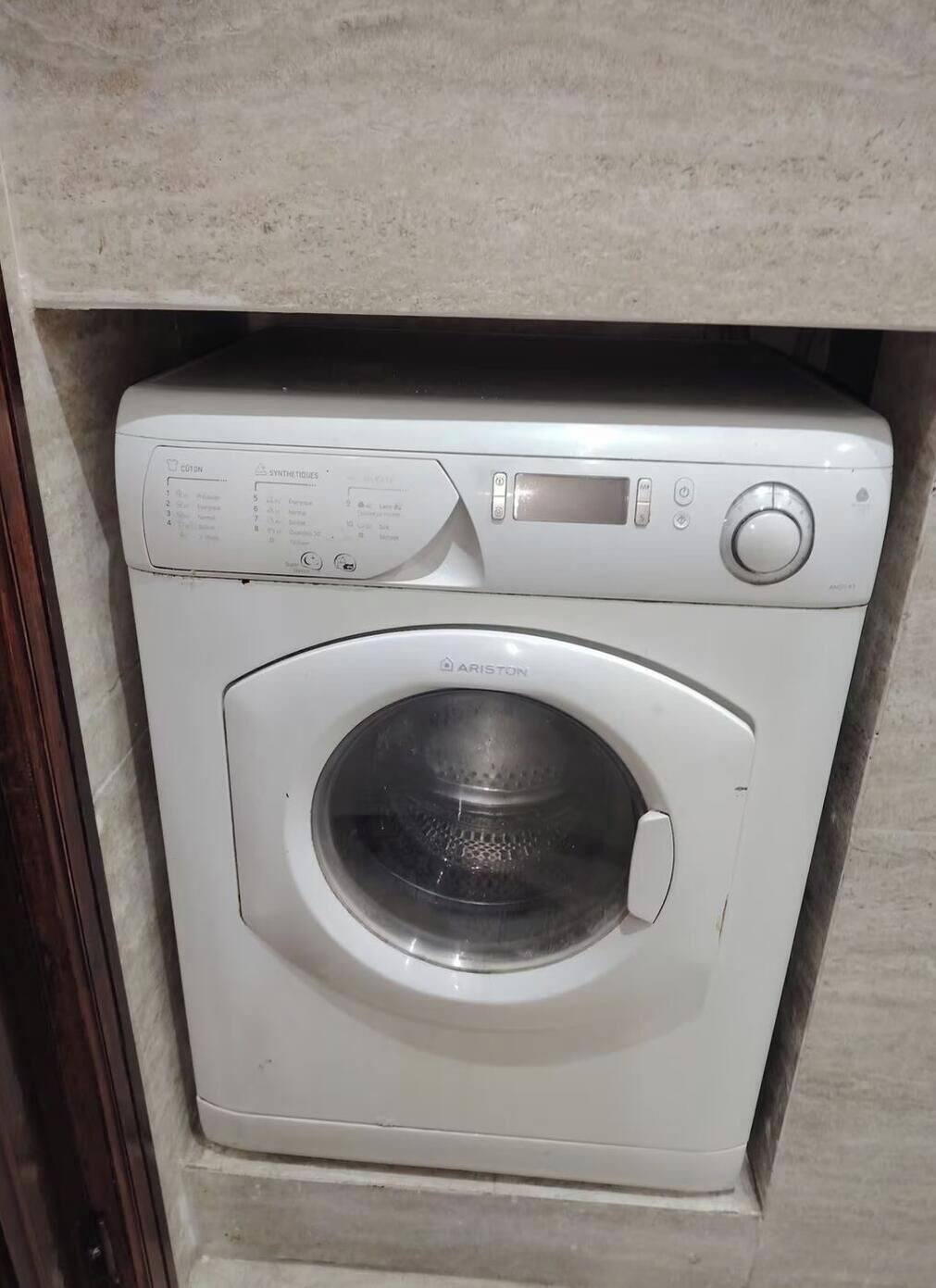 A white Ariston washing machine in a built-in cabinet.