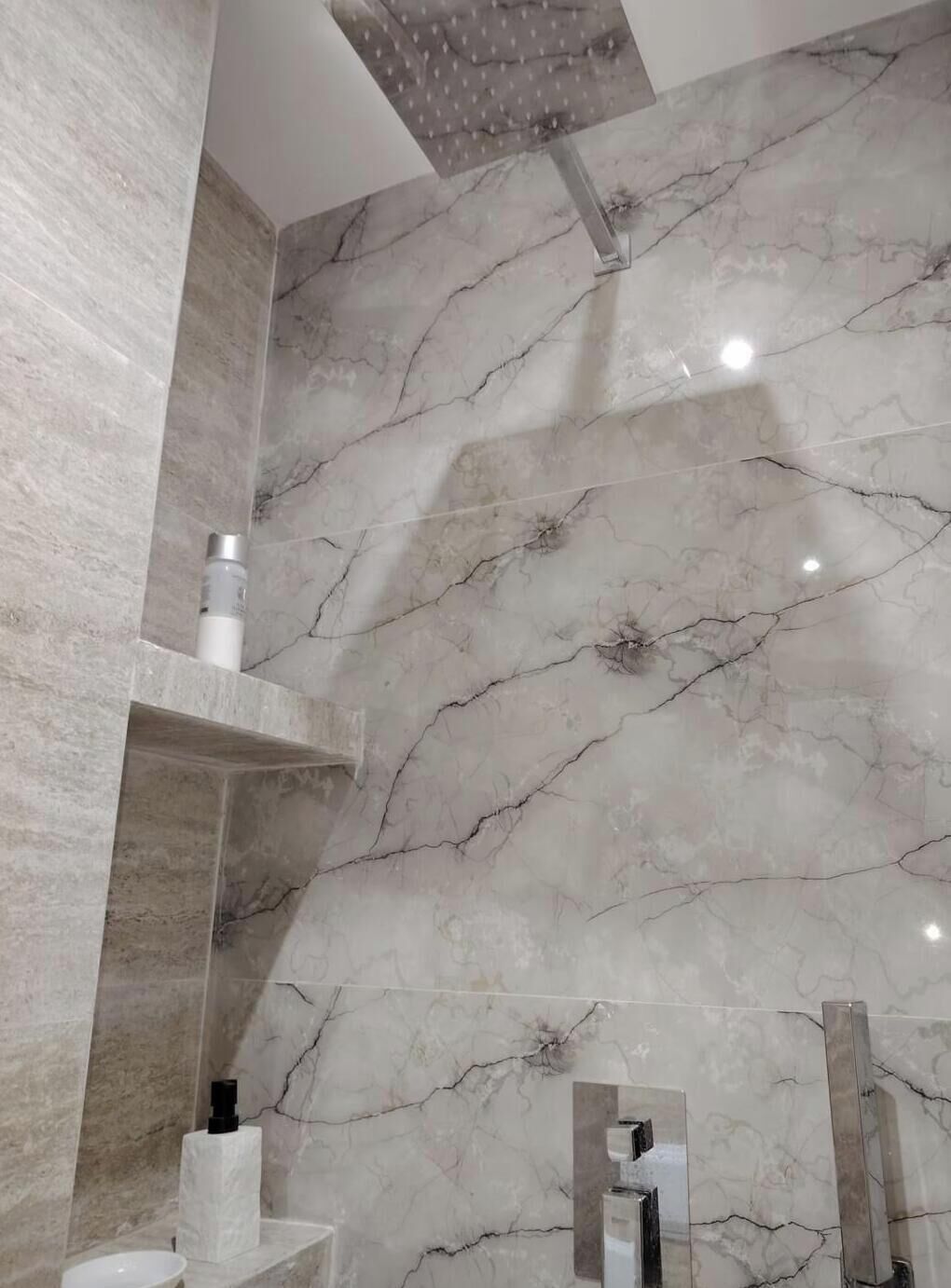 Un baño con paredes de mármol, ducha e inodoro.