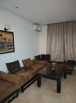 A living room with a brown sofa, a glass coffee table, and a painting on the wall. - Marrakech wintering chic apartment ideally located (Marrakesh)