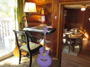 Ein Zimmer mit Klavier, Gitarre, einem Sessel, einem Tisch mit einer Schüssel und einem an der Wand montierten Feuerlöscher.