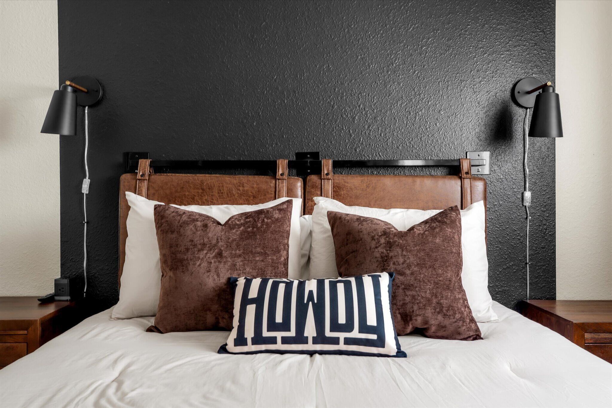 Ein Bett mit Kopfteil, zwei Nachttischlampen und einem Kissen mit dem Schriftzug 'HONEY'.