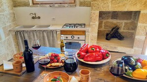 Una cocina rústica con pared de piedra, estufa a gas, lavabo y mesa de madera dispuesta con comida y bebidas.