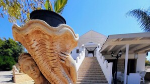 Una estatua con una olla grande en la cabeza, una escalera que conduce a un edificio y asientos al aire libre.