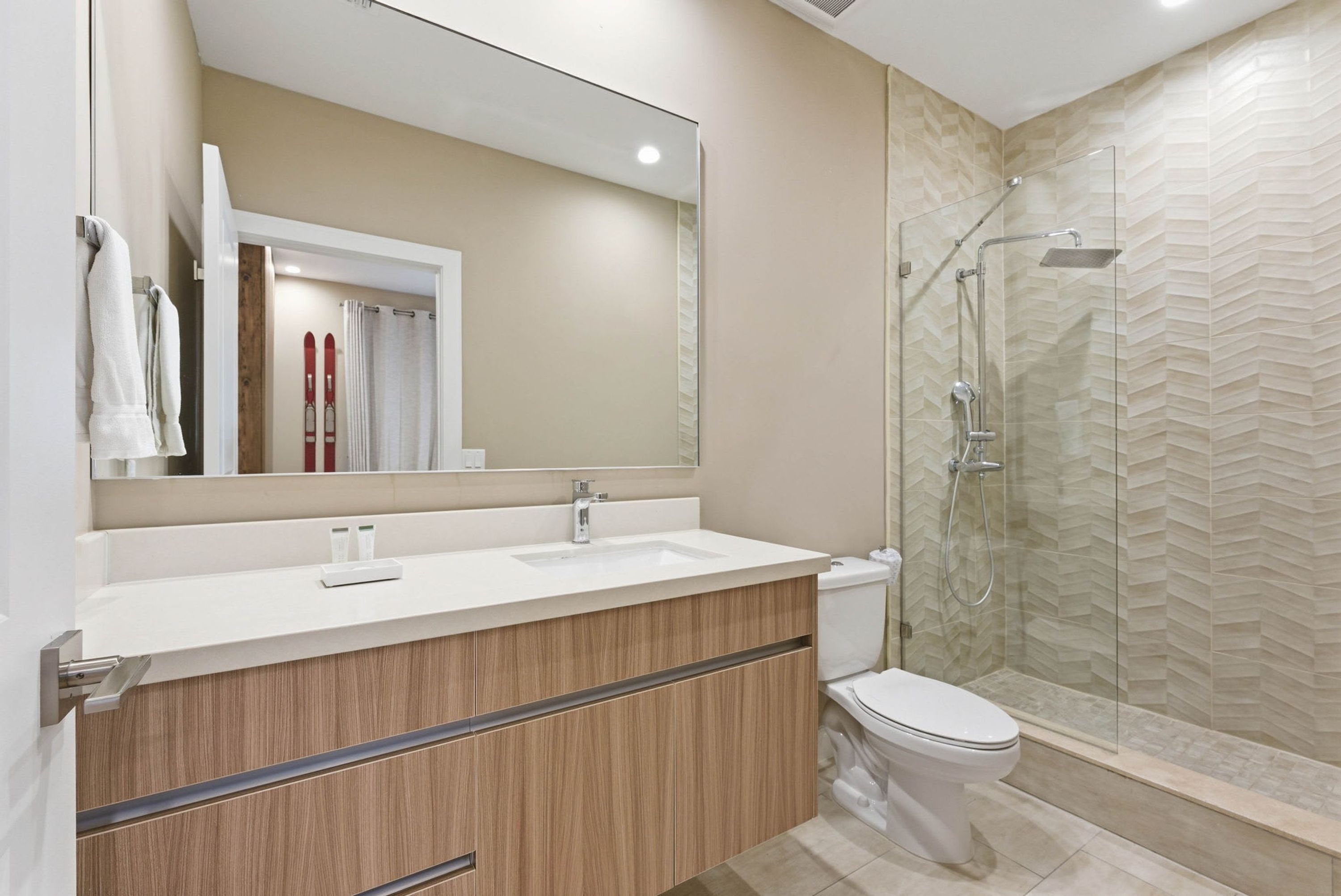 A modern bathroom with a large mirror, a sink, a toilet, and a glass-enclosed shower.