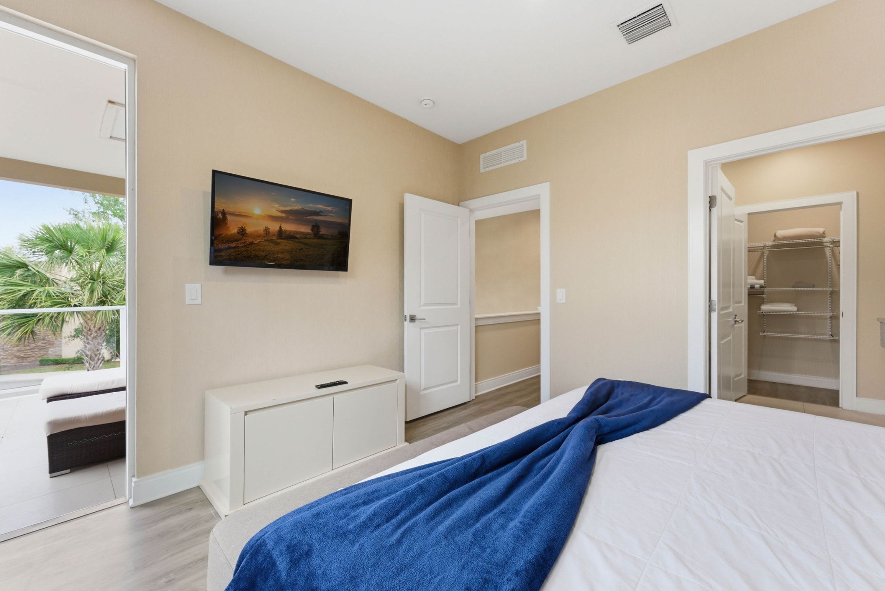 A bedroom with a bed, a painting, a closet, and a door leading to a balcony.