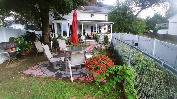 En terrasse med et bord og stole, omgivet af krukker med planter og en rød parasol.