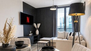 A modern living room with a flat-screen TV, a sofa, a coffee table, and a floor lamp. - Modern City Centre Flat | Balcony & Free Parking (Birmingham)