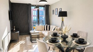 A modern dining area with a glass table, black bowls, and white chairs. - Modern City Centre Flat | Balcony & Free Parking (Birmingham)