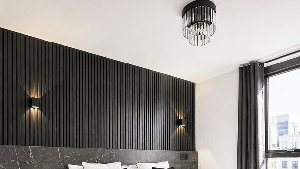 A modern hotel room with a large bed, black and white bedding, a marble headboard, and a city view. - Modern City Centre Flat | Balcony & Free Parking (Birmingham)