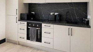 A modern kitchen with a black marble backsplash, stainless steel appliances, and light-colored cabinetry. - Modern City Centre Flat | Balcony & Free Parking (Birmingham)