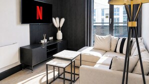 A modern living room with a TV mounted on the wall, a sofa, a coffee table, and a floor lamp. - Modern City Centre Flat | Balcony & Free Parking (Birmingham)