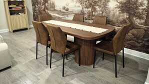 Un coin repas comprenant une table ronde, six chaises, une bibliothèque et une fresque représentant un paysage.