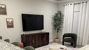 Un salon avec un téléviseur, une plante, un canapé et un coin repas avec des chaises.