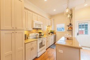A kitchen with white cabinets, a microwave, a stove, and a sink. - Historic District Haven • Collected & Comfortable (Temple)