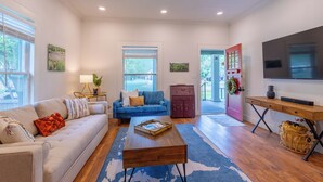 A living room with a sofa, coffee table, TV, and a red door leading outside. - Historic District Haven • Collected & Comfortable (Temple)