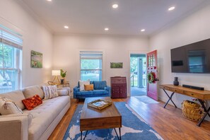 A living room with a sofa, coffee table, TV, and a red door leading outside. - Historic District Haven • Collected & Comfortable (Temple)