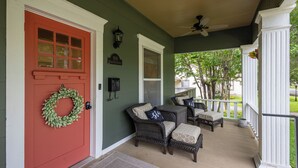 A porch with wicker furniture, a red door, and a green wall. - Historic District Haven • Collected & Comfortable (Temple)