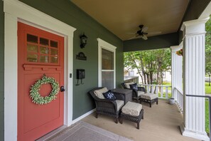A porch with wicker furniture, a red door, and a green wall. - Historic District Haven • Collected & Comfortable (Temple)