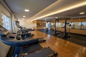 Ein Fitnessraum mit Laufbändern, einer Gewichtbank und einer Spiegelwand.
