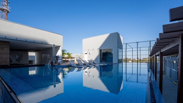 En swimmingpool med kristallklart blått vatten, ett avskärmat område med solstolar och en modern byggnadsstruktur.