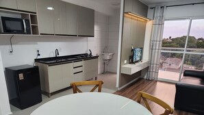 Ett modernt kök med mikrovågsugn, spis och diskho, en matplats med ett runt bord och stolar samt ett stort fönster med utsikt.