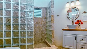 Un baño con cabina de ducha de vidrio, un lavamanos blanco con un florero y un espejo sobre el lavamanos.